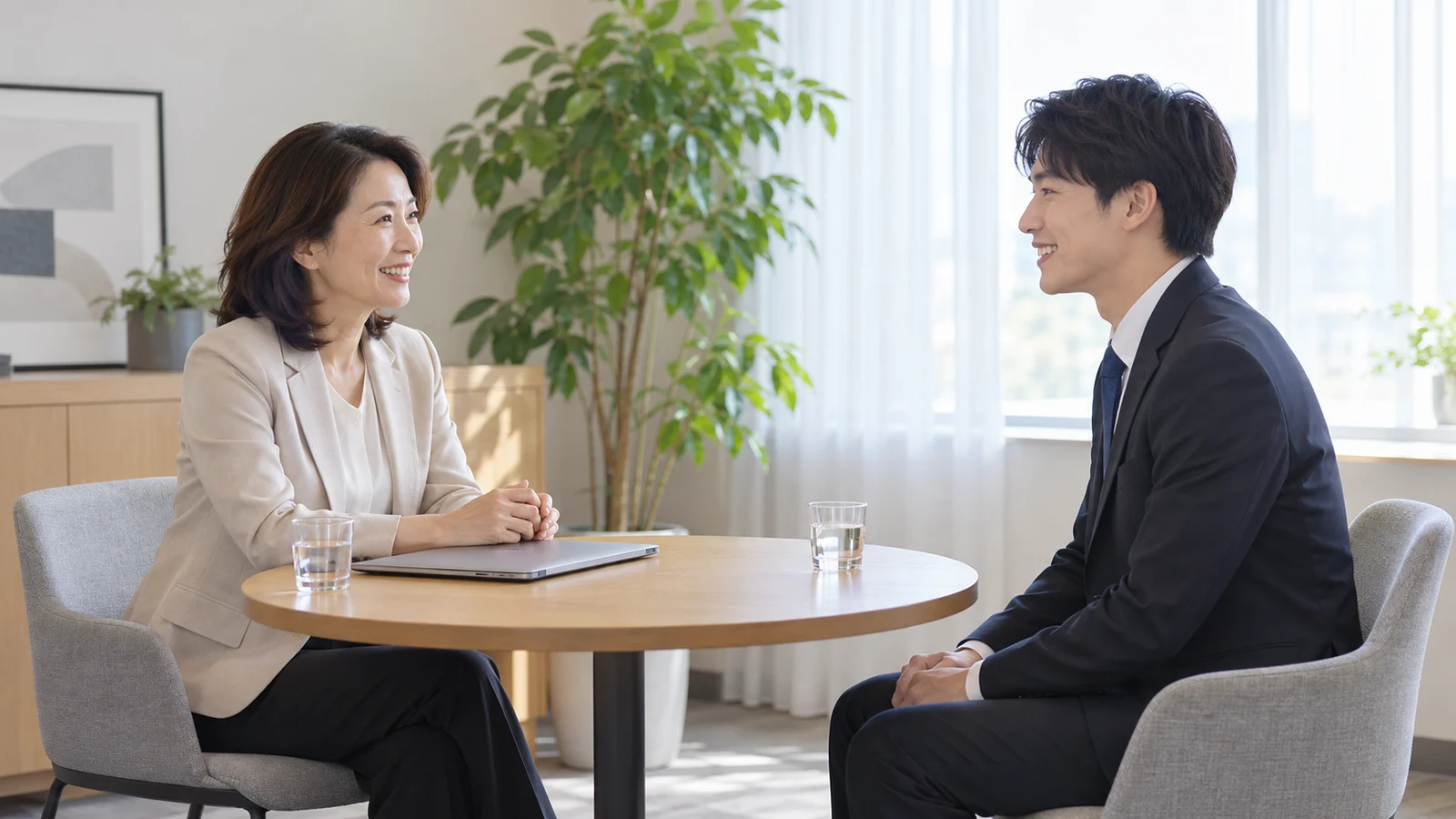 明るい面談室の丸いテーブルで、人事の担当者が応募者と向き合って話している様子