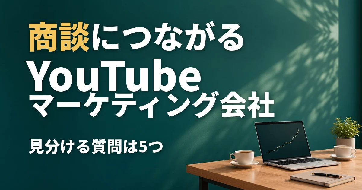商談につながるYouTubeマーケティング会社。深い緑の壁の前の木の机に、ノートパソコンとコーヒーカップとノートが置かれている